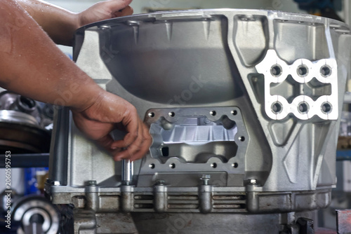Obraz na plátně Close-up of mechanic hands tightening bolt on a clean aluminum car gearbox housing casing using a socket wrench tool in an auto repair shop workshop