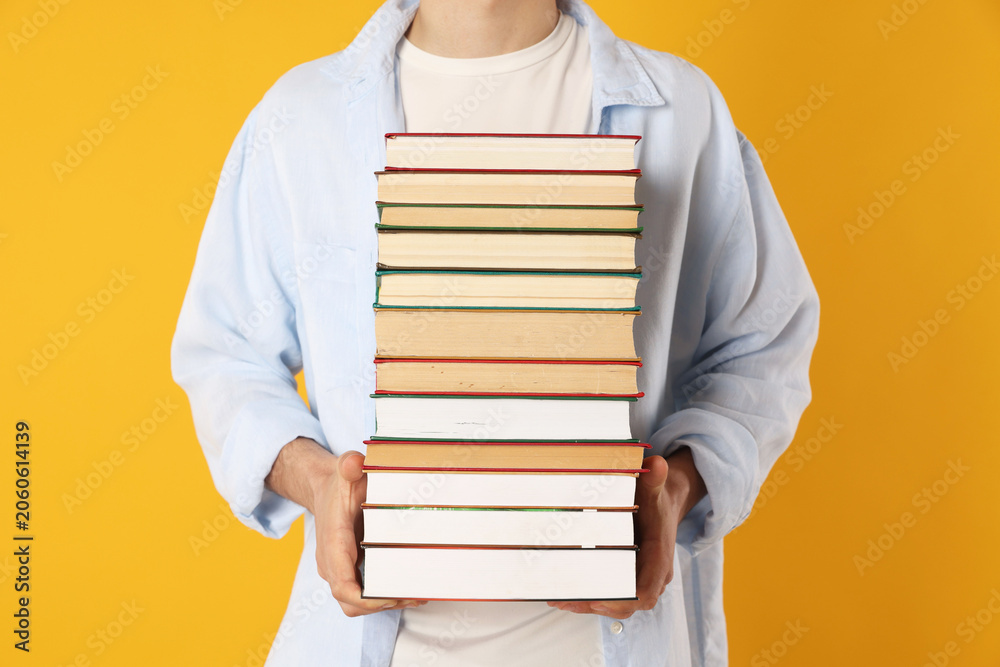 Fototapeta premium Teenage boy with stack of books on orange background, closeup