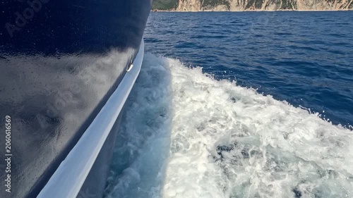 Close-up view of a passenger ferry moving through the Ionian Sea near the Greek islands. White water splashes and foamy waves flow alongside the vessel hull, creating a dynamic maritime travel