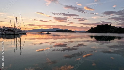 Atmospheric sunrise scene in Lefkada, Greece, featuring a small boat approaching a marina across calm reflective water. 