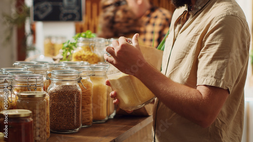 Photos Man in zero waste supermarket thoroughly checking products before making purchase decision, making sure they are natural, customer verifying pantry staples displayed in local store are organic
