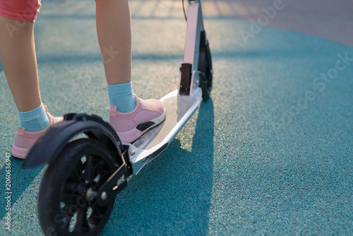 Close up of child legs riding kick scooter on playground