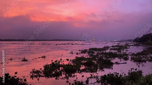 Dramatic pink and purple sunset reflecting on a calm Magdalena river, with floating aquatic plants and a distant horizon creating a serene tropical waterscape.
