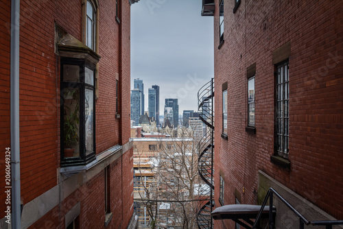 View of Montreal skyline and downtown CBD from between red brick residential buildings, showing urban housing, business towers and real estate density in a North American city in Quebec and Canada.