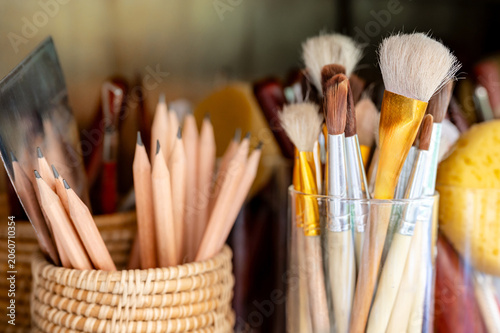 Various artist paintbrush with pencils, painting spatula and sponge grouping in the glass holder in art workshop studio. Art paint tools supplies for creativity class