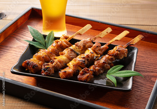 Japanese Yakitori Chicken Skewers with Blurred Glass of Beer on Wooden Tray