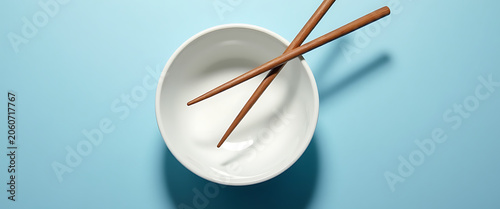 Empty white bowl with wooden chopsticks on blue background.