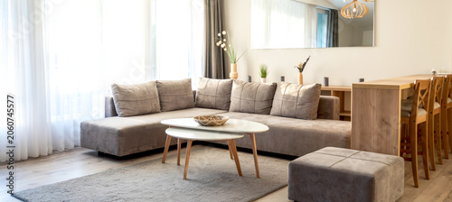 Modern living room with gray sectional sofa, white coffee table, wooden dining area, and natural light