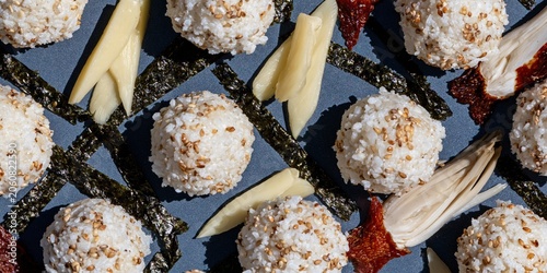 Temari rice balls with sesame seeds and nori strips on a dark surface, a minimalist Japanese food pattern for backdrop and culinary design