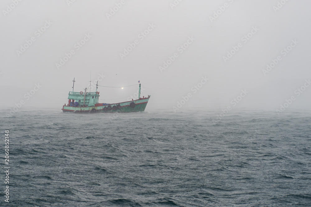 Fototapeta premium Traditional Thai Fishing Boat Navigating Through Heavy Rain and Rough Seas in the Gulf of Thailand. A weathered local fishing boat travels across choppy ocean waters during heavy rain in Thai sea.