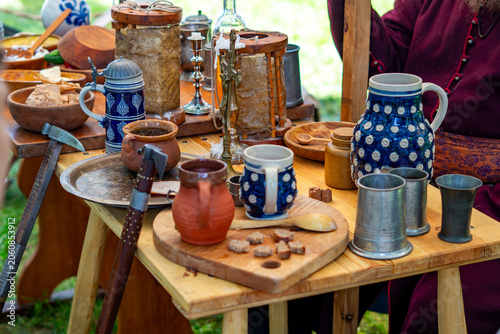 Schilderij op canvas Historical replica tableware, including ceramic pottery, clay jugs, pewter mugs, wooden spoons, and bread pieces arranged on a wooden table during a reenactment festival