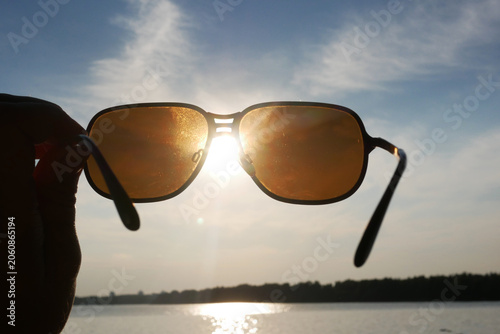 Hand holds sunglasses against setting sun