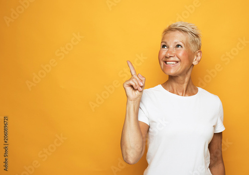 Senior grey-haired woman pointing finger up with successful idea over yellow background.