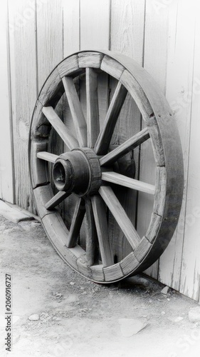Old wooden wagon wheel resting against a rustic weathered wooden plank wall