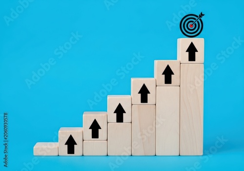 Wooden blocks arranged as a staircase with upward arrows and a target icon on top representing business growth and success
