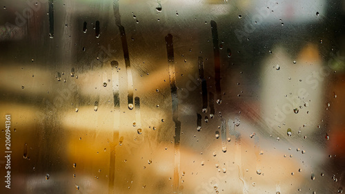 Raindrops on a window pane with soft bokeh background light for a moody rainy day texture and tranquil indoor atmosphere