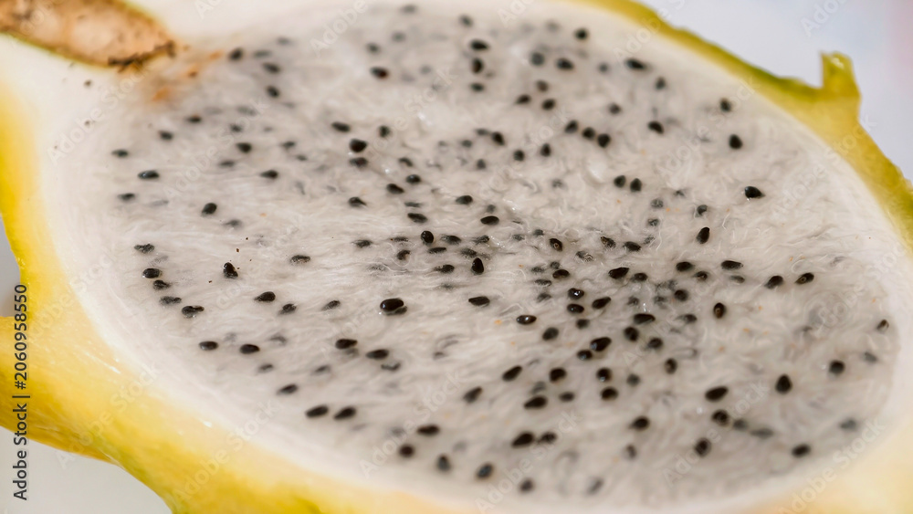 Obraz premium Close-up of a vibrant yellow pitaya, also known as dragon fruit, revealing its striking white flesh generously dotted with tiny black edible seeds, showcasing its unique tropical texture and appeal