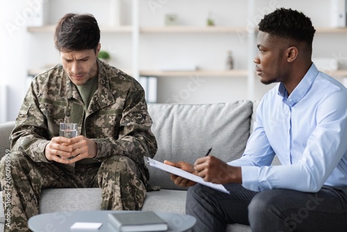 Foto Worried Male Soldier In Military Uniform Attending Therapy Session With Black Male Therapist In Professional Office Setting