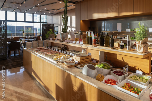Modern hotel buffet station with fresh salad bar and cold cut platters in morning sunlight