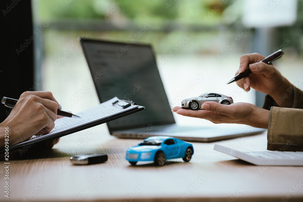 Fototapeta premium Close-up of a car sales or leasing consultation, with a miniature vehicle presented to a customer, symbolizing auto financing, ownership transfer, vehicle purchase, and rental services.