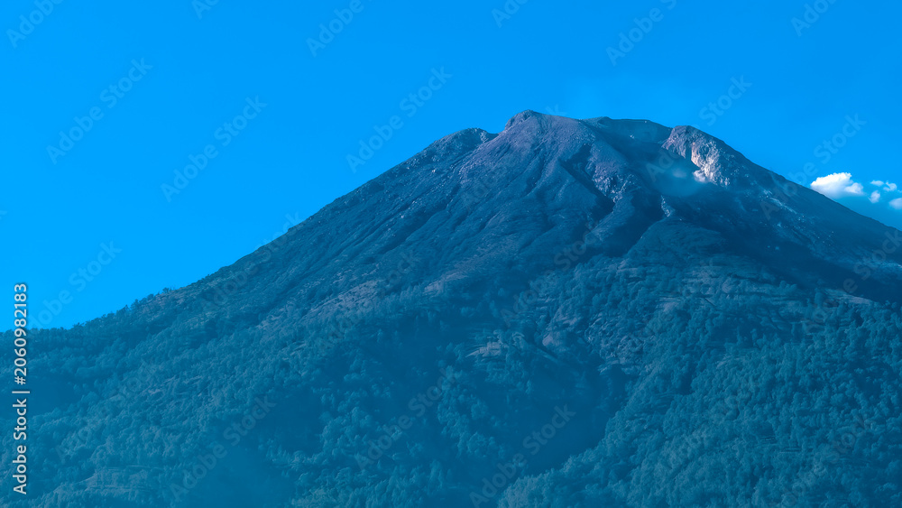 Fototapeta premium Majestic Volcano Peak Rising into a Clear Blue Sky with Forested Slopes Below
