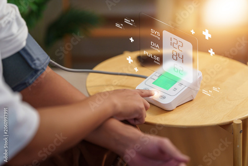 Photos Cropped hand pressing button on digital blood pressure monitor at home for cardi