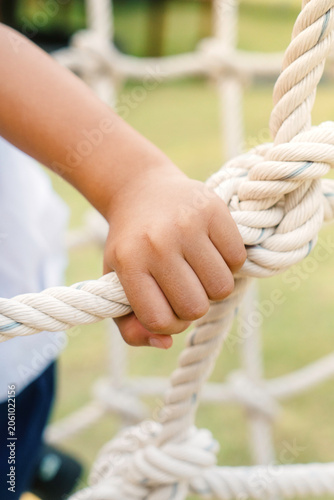 Close-up of a child’s hand holding a rope climbing structure at an outdoor playground. Concept of physical development, balance, confidence, motor skills, and active learning.