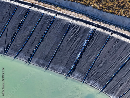Black geomembrane slope with blue pipes beside greenish mine tailings pond