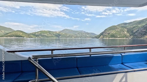Peaceful view from a passenger ferry deck crossing the Ionian Sea near Lefkada, Greece. Comfortable seating area overlooking calm blue water and mountainous islands under a bright summer sky. 