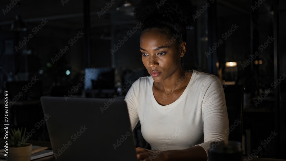 Fototapeta premium Woman working on laptop late at night in dark office.