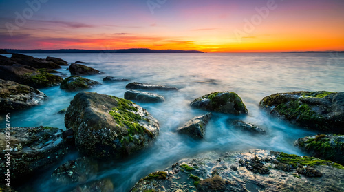 Serene rocky coastline at sunset with vibrant sky and mossy boulders