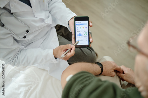 Fotografie Senior patient visiting doctor in clinic, reviewing glucose monitoring app on smartphone during consultation