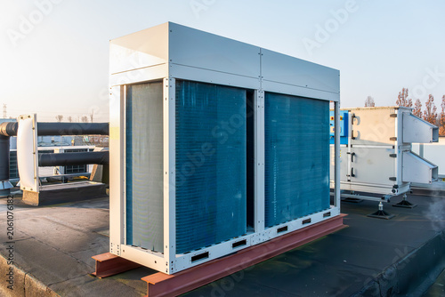 A modern industrial HVAC chiller system and large air conditioning condenser units installed on a flat commercial building rooftop. 