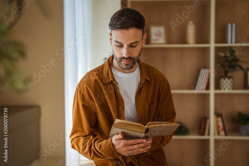Fényképezés Young man concentrating while reading a book at home