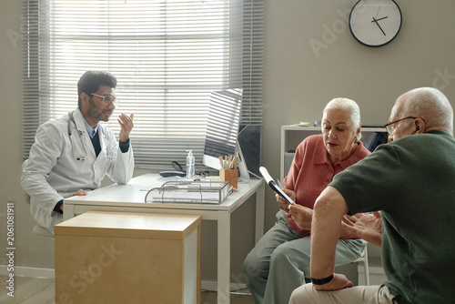 Senior couple visiting doctor in clinic, discussing medical document during consultation and treatment planning. Ideal for healthcare access, patient care, insurance marketing