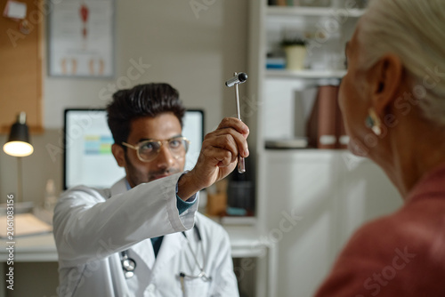 Senior woman visiting doctor, following reflex hammer during neurological exam in clinic, showing preventive healthcare and diagnosis. Ideal for senior care, medical services marketing