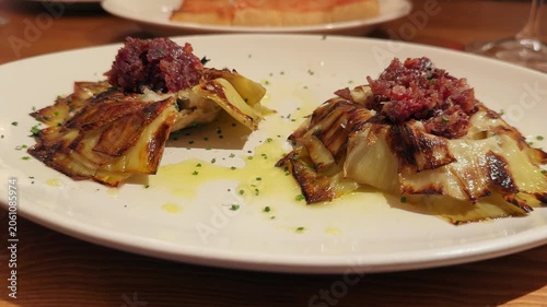 A close-up of fried artichoke blossoms served on a plate, drizzled with olive oil and topped with crispy ham. Authentic Mediterranean cuisine.