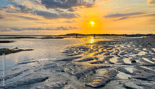 This scene likely depicts a sunset over a tidal flat or beach with exposed sand and shallow water reflecting the golden sky.