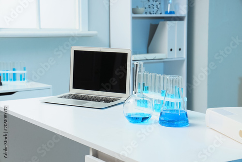 Modern laboratory workspace with laptop and blue liquid in glassware, scienti...