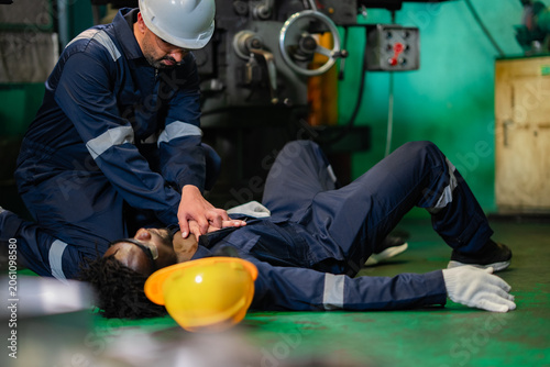 Fényképezés Factory employee administering cardiopulmonary resuscitation to injured coworker on workshop floor