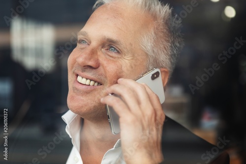 Fényképezés Smiling man talking on a smartphone, wearing a white shirt, indoors