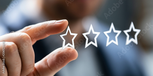 Businessman holding five-star rating icon between his fingers, symbolizing customer feedback, quality service, and business excellence.