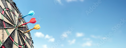 Dart in bullseye of dartboard with blue sky background  hitting target, goal and success