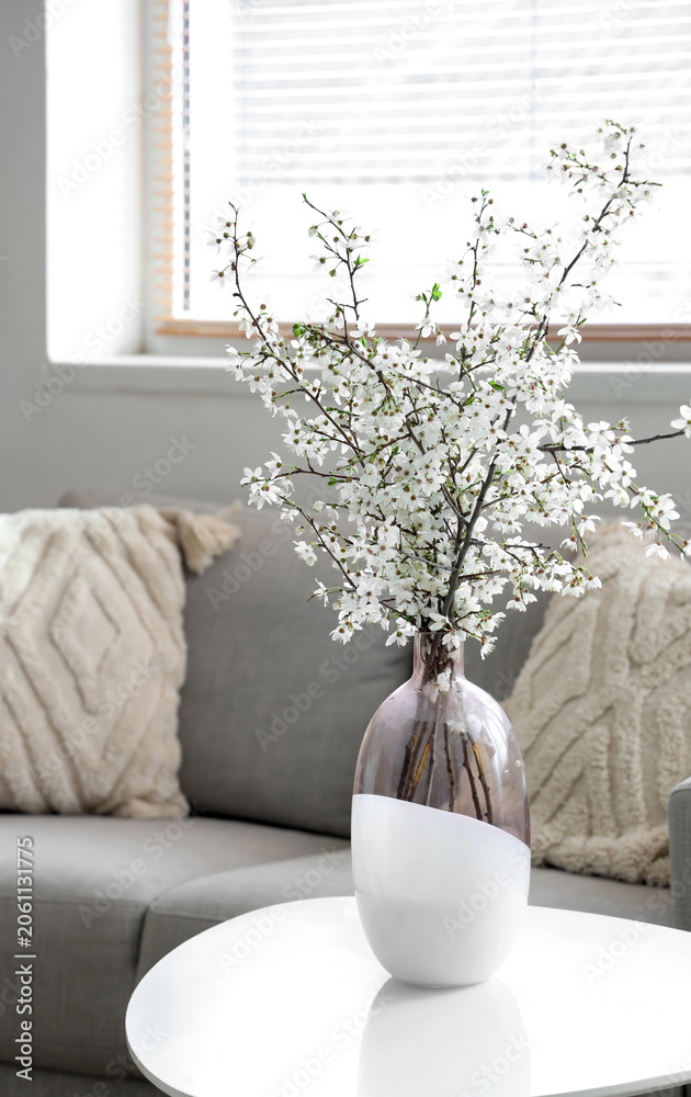 Obraz premium Vase of blooming branches on coffee table near sofa in living room