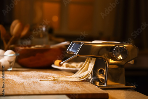 Bild auf Leinwand Pasta machine with dough on table in dark kitchen, closeup
