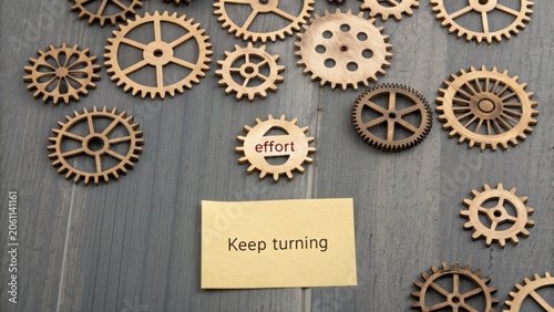 Wooden Gears on Table with Note Reminding to Keep Turning and Focus on Effort in a Motivational and Creative Context