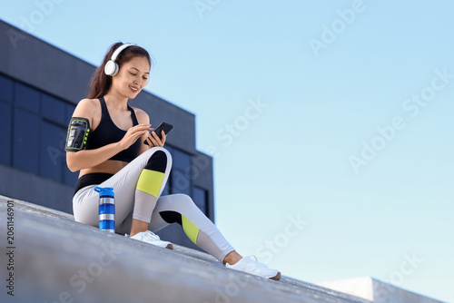Young sporty Asian woman in headphones with fitness tracker, bottle of water ...