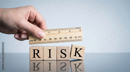 Wooden blocks spelling RISK are being measured by a ruler held by a hand, symbolizing assessment and management of risk.
