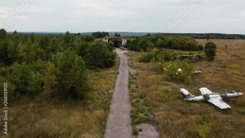 Aerial view of abandoned airbase field with retired airplanes and weathered hangar surrounded by natural greenery