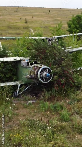 Aerial arc of weathered An-2 airplane abandoned in overgrown airfield, aircraft remains in summer